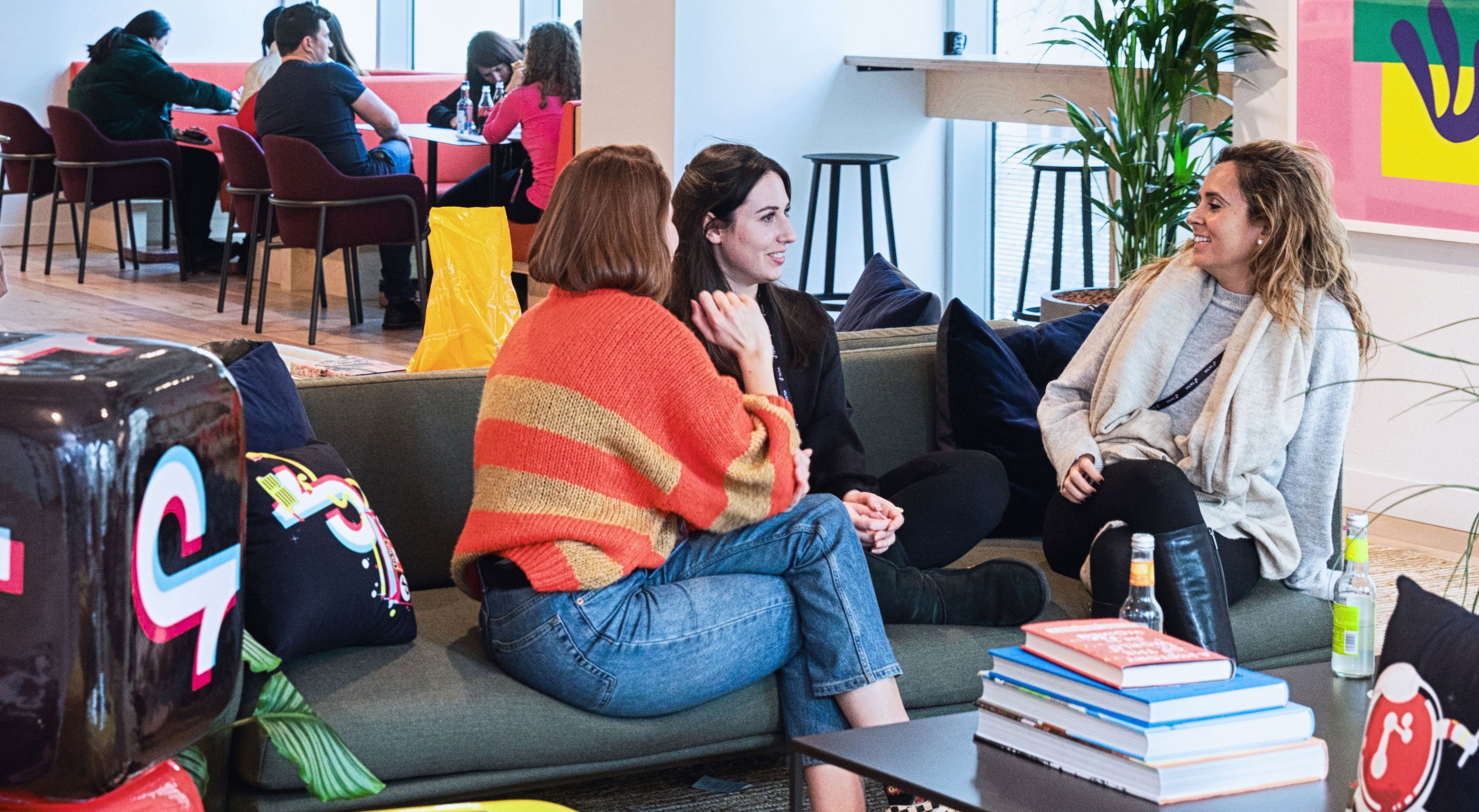 Three TikTok female employees sit on a couch as they talk amongst themselves in the office..