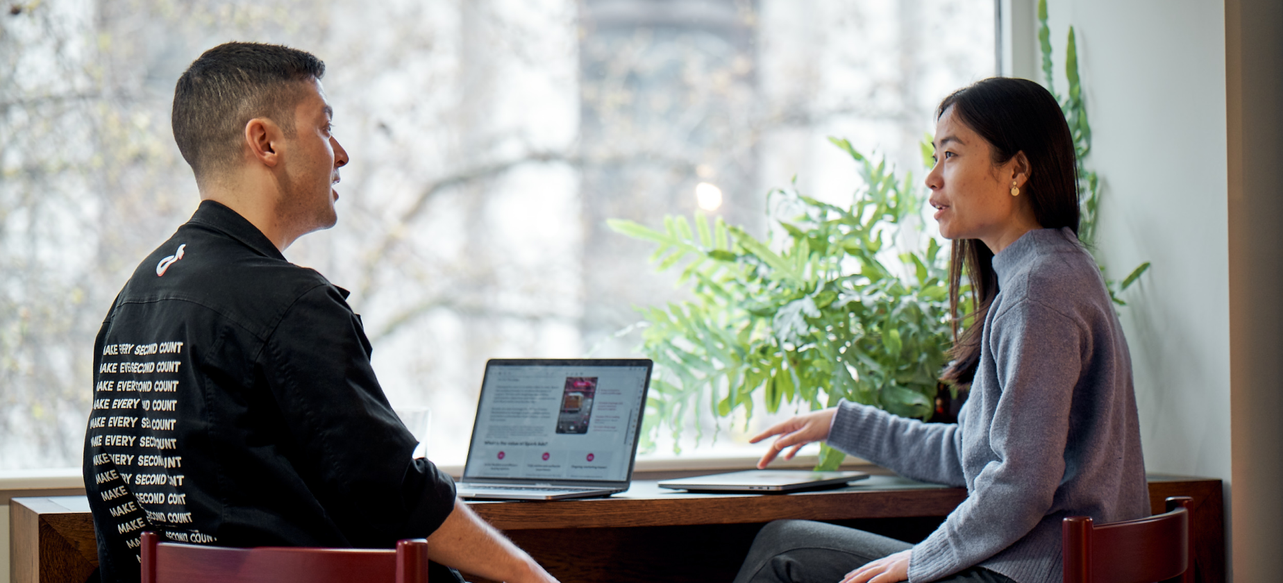 A male and a female TikTok employee sit and talk with an open laptop next to them.