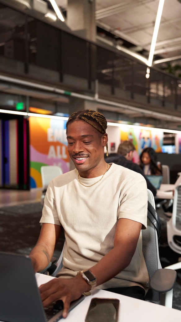 A young Black TikTok employee smiles as he works at his computer.
