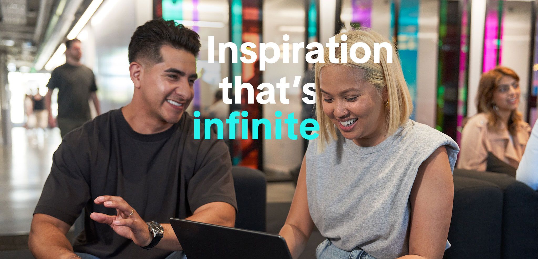 A male and a female TikTok employee talk and smile as they sit beside each other and work on a project together.