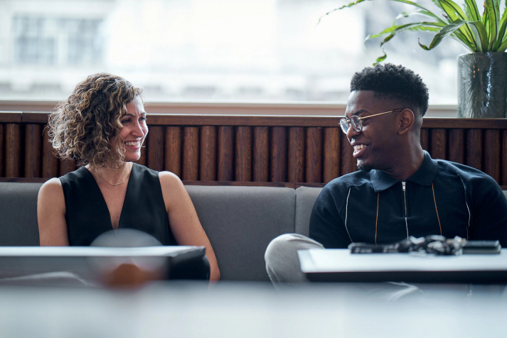 A young male and a female TikTok employee smile as they sit beside each other on a couch.