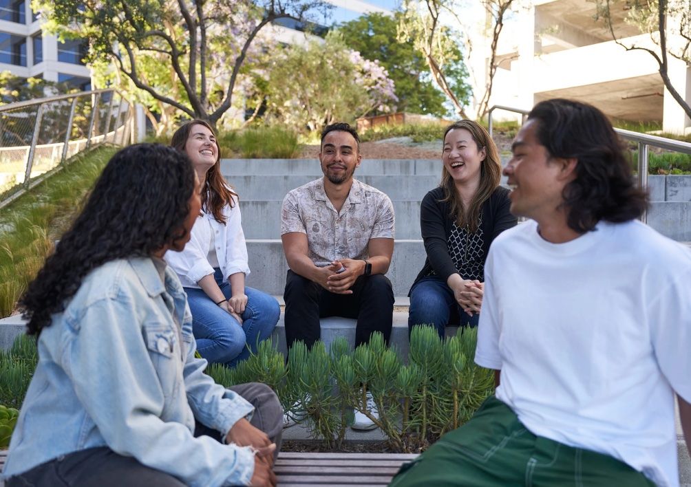 A diverse group of employees at a TikTok office in North America sit outside laughing and talking together.