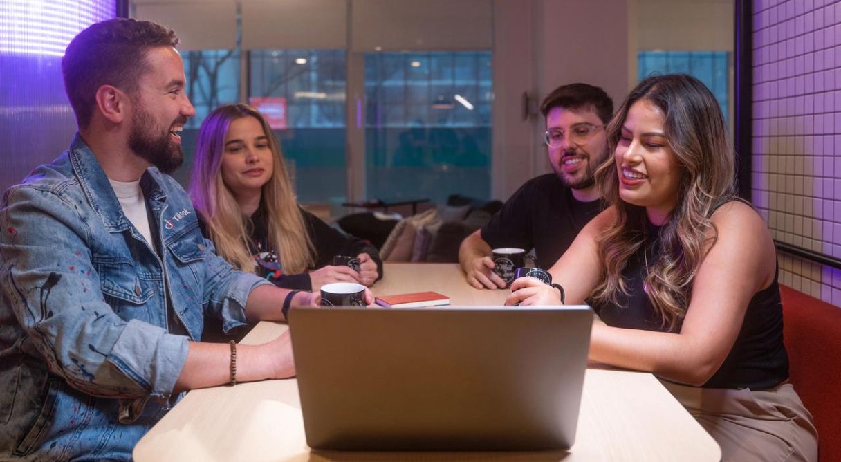 Four TikTok Latin America Internship Program attendees sit at a desk and look at the screen of an open laptop.